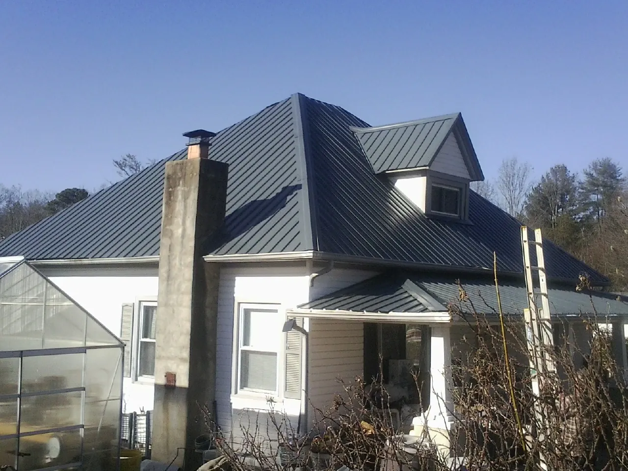 Dark blue standing seam metal roof on a white farmhouse with dormer — Slate & Tile Roof Repair by Roofing Brothers in Steinauer