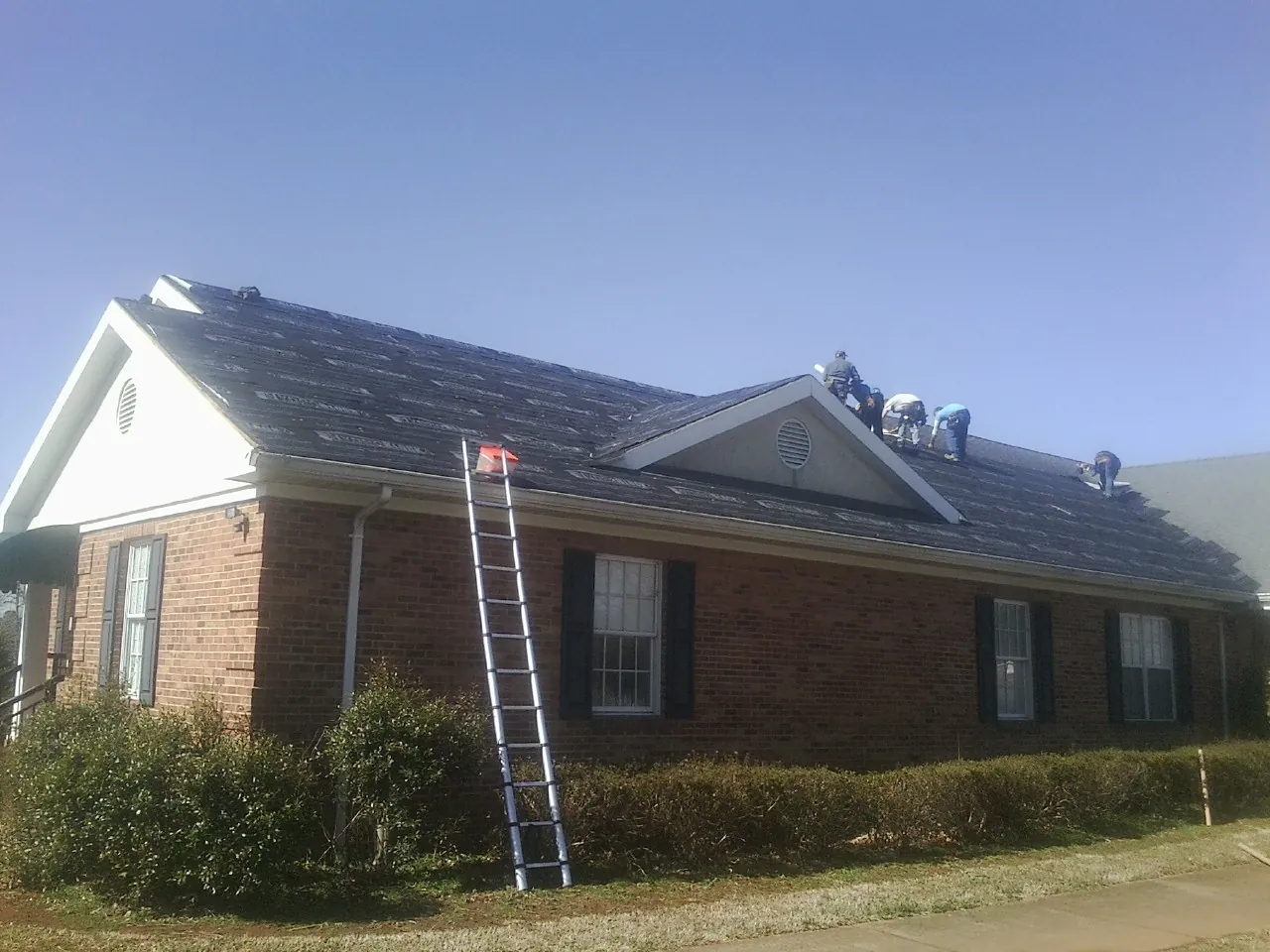 Crew tearing shingles off a brick ranch roof with a ladder set — Emergency Roof Repair work by our crew in Steinauer