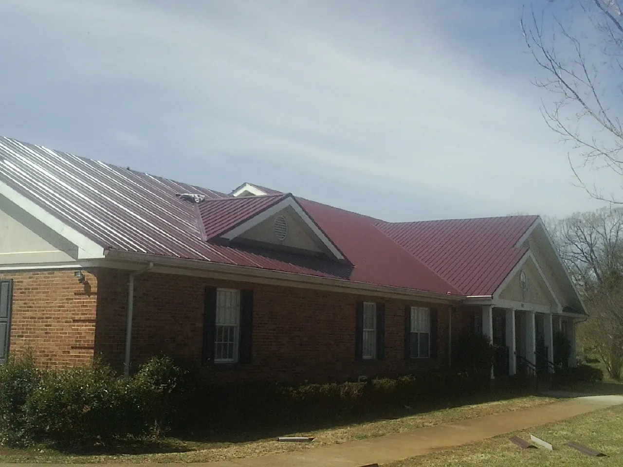 Red metal roof with gabled entries on a long brick building, from a Hail Damage Roof Repair job in Steinauer