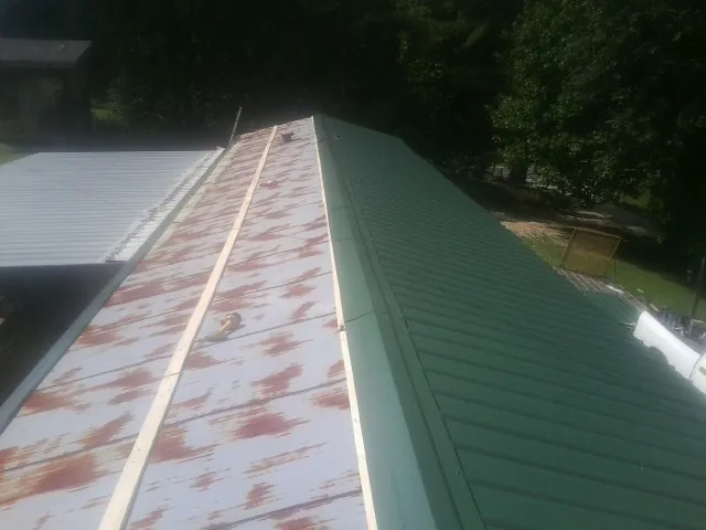 Old rusted panels beside newly installed green metal roofing — Wind Damage Roof Repair by Roofing Brothers in Steinauer