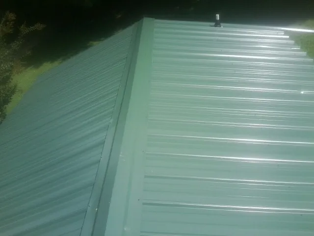 New green metal panels meeting at the ridge of a roof — Flat Roof Repair work by our crew in Steinauer